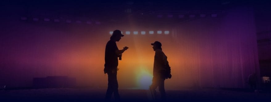 ICLS-background Two lighting engineers are silhouetted against a glowing light