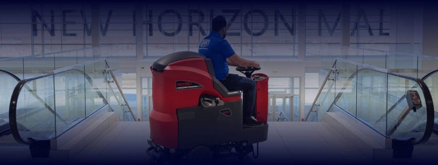 Cleaner driving a ride-on floor scrubber between escalators